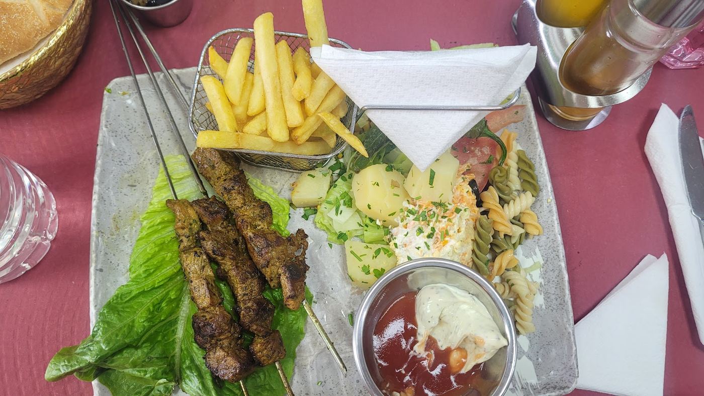 Brochetas de carne a la parrilla servidas con patatas fritas y ensaladas.